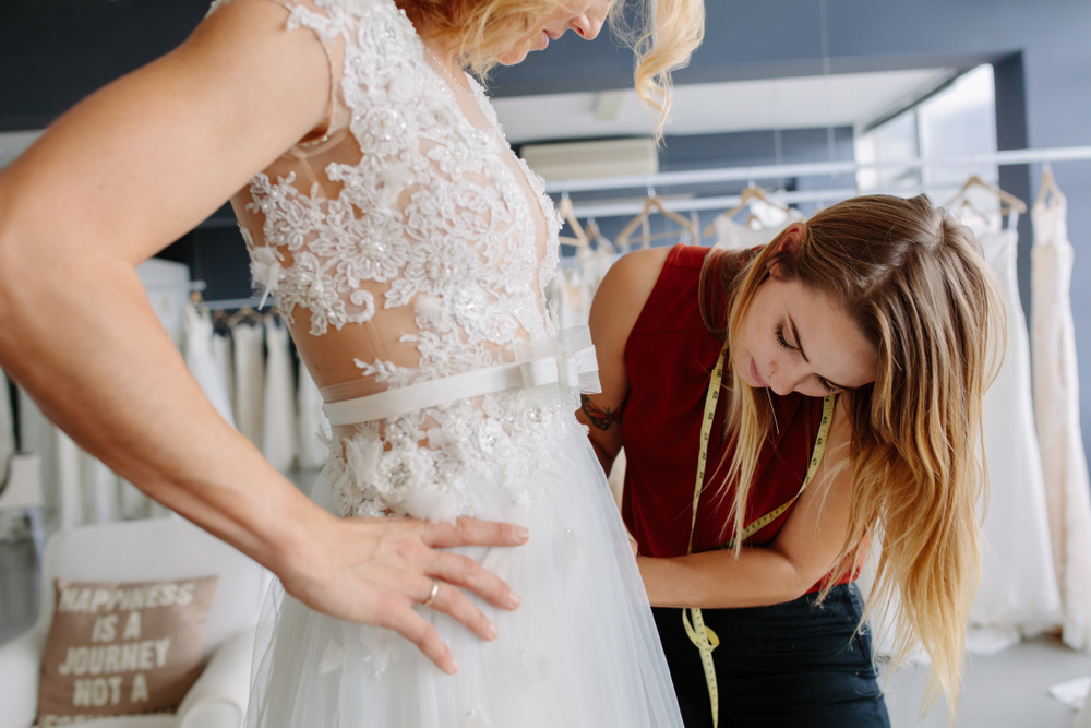Skillful dress designer fitting wedding gown to woman in her boutique